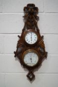 An early 20th century oak wall clock/barometer, the framed ornately carved as foliage and branches,