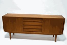 A mid-20th century teak sideboard with four central drawers flanked by cupboards with sliding doors,