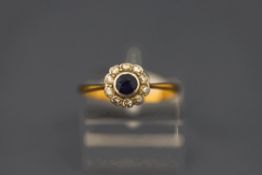 A sapphire and diamond cluster ring, stamped '18 ct', the round cut enclosed by single cut diamonds,