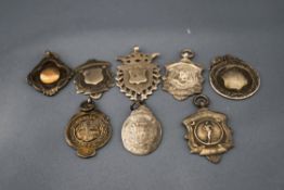 A collection of right silver watch fobs, including one depicting a runner,