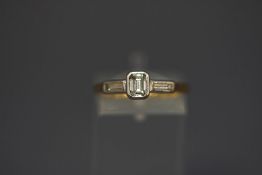 An 18 carat gold three stone diamond ring, the central step cut of approximately 0.