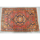 A rug with central medallion on a red field with black ground spandrels within three boards,