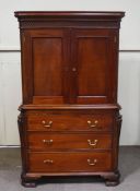 A reproduction George III style mahogany cupboard over three long drawers with carved cantered