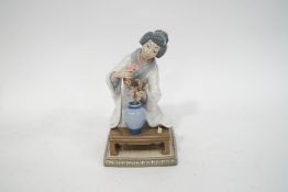 A Lladro figure of a Japanese lady in traditional dress, arranging flowers in a vase,