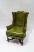 A green leather wing back armchair, with turned legs joined by an 'X' frame stretcher,
