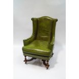 A green leather wing back armchair, with turned legs joined by an 'X' frame stretcher,