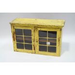 A rustic painted pine wall cabinet, with square panes to the glazed doors,