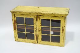 A rustic painted pine wall cabinet, with square panes to the glazed doors,