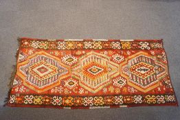 A Turkish kelim with three central medallions and repeating motifs to central field on a red ground,