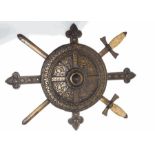 A cast iron wall plaque in the form of a shield in front of a Crucifix and two swords,