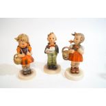 Three Hummel figures, two girls with baskets and a singing boy,