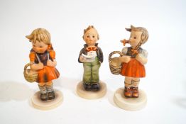 Three Hummel figures, two girls with baskets and a singing boy,