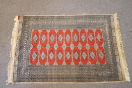 A Middle Eastern rug with central repeating diamond motif to a red ground,