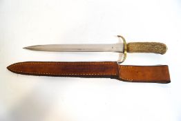 A horn handled hunting knife in leather sheath with tooled decoration,