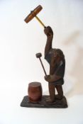 A carved figure of a monkey holding drumsticks and beating a lidded barrel,