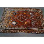 A Middle Eastern rug, the central field with three rows of diamond motifs over a rust red ground,