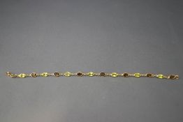 A 9 carat gold bracelet, alternate spectacle set with oval cut peridots and smoky quartz,