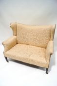 An Edwardian two seat wing back sofa, with foliate patterned upholstery,
