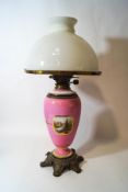 A 19th century porcelain oil lamp painted with landscapes within gilded line borders on a pink