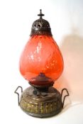 A two handled oil lamp with cranberry tinted glass shade and embossed round brass effect reservoir,