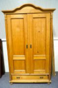 An Edwardian pine double wardrobe, with shaped top above two panelled doors and a single drawer,