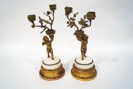 A pair of French style gilt metal and marble twin branch candlesticks, cast as cherubs,