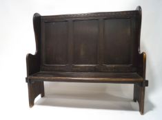 An oak settle with carved frieze above the triple panelled back and plank seat. 119cm high x 128.