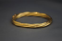 A yellow metal hinged bangle, of twist design,