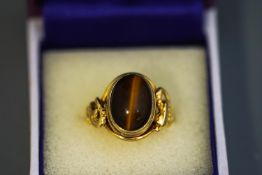 A tiger eye ring, unmarked, the cabochon between entwined serpent shoulders, finger size J, 6.
