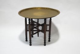 An Indian brass tray table with folding wooden stand,