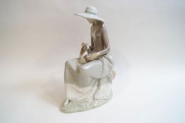A large Lladro figure of a seated lady in a wide brimmed hat, with a dog on her lap,