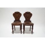A pair of Victorian oak hall chairs, the shaped backs with carved scroll detail,
