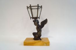 A painted bronze figure of a kneeling putti, holding aloft a six sided glass lantern,