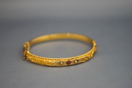 A Victorian unmarked gold hinged bangle, set with a red doublet and two seed pearls,