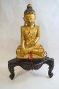 A carved and gilded figure of Buddha, 62cm high, on a stained wood stand,