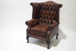 A 20th century leather wing button back armchair on cabriole legs,
