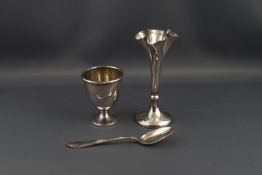 A silver egg cup and spoon, and quatrefoil spill vase on a loaded round base, 10.