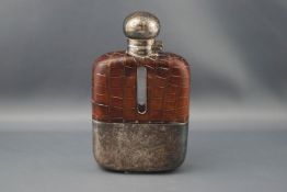 A clear glass oblong hip flask with crocodile effect brown leather mounts and a plated hinged cover