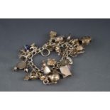 A silver charm bracelet with a padlock clasp and approximately 30 charms including a blue enamelled