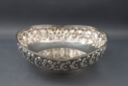 A white metal round bowl with undulating rim, embossed with a band of repeating flowerheads,