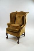 A George III style wing back armchair with carved front cabriole legs on claw and ball feet,