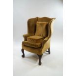 A George III style wing back armchair with carved front cabriole legs on claw and ball feet,