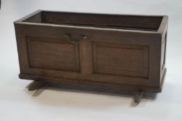 An 18th century oak cot with panelled sides and ends, containing a lead planter liner,