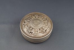 A Chinese white metal round box and cover embossed with bats on a textured ground and with a beaded