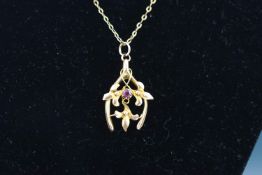 An Edwardian rose gold and ruby pendant in the form of a horseshoe entwined with flowers and leaves,