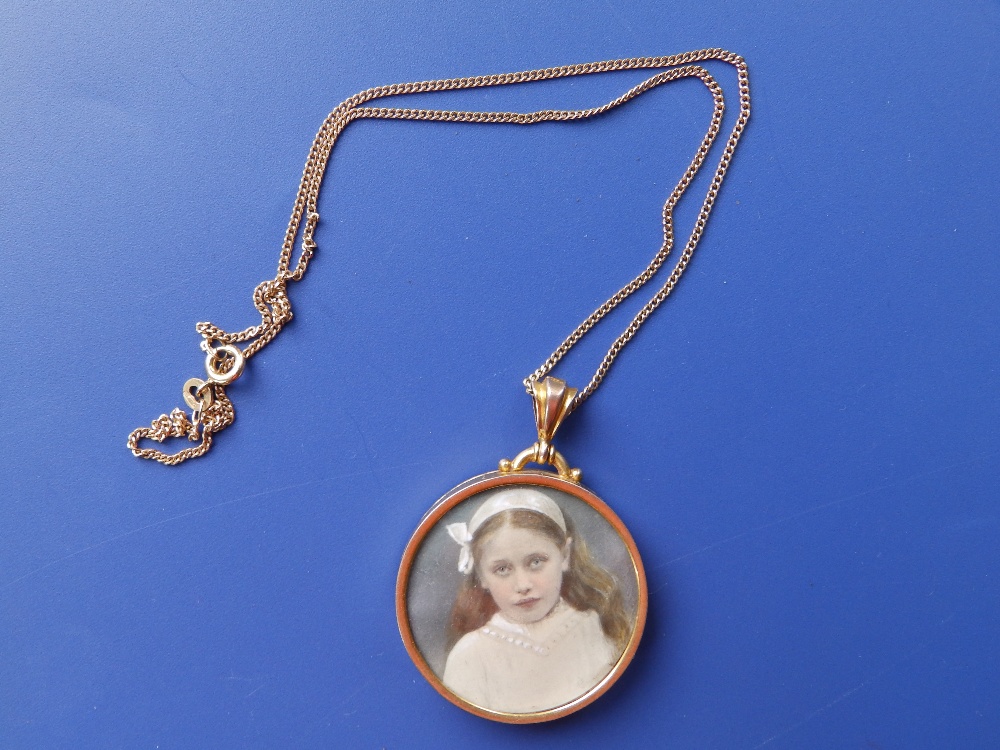 A circular yellow metal glazed locket on chain.