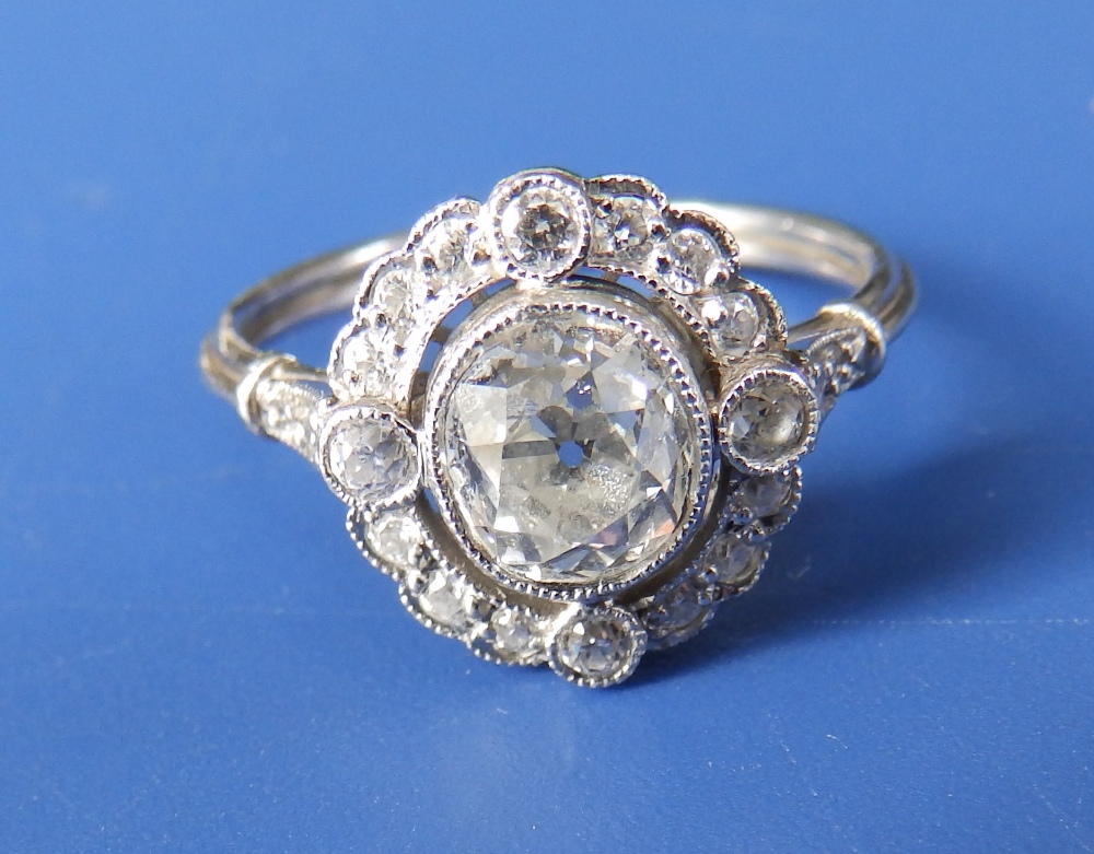 An oval diamond millegrain set open cluster ring, the central old cut stone weighing 1.10 carats –