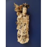 A Japanese stained ivory figure of a Bijin carrying an ikibana basket with peony arrangement on