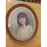 A small oval early 20thC watercolour portrait of a young girl with a red bow in her hair.