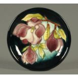 A Moorcroft plate, with dark green and blue ground and decorated with orchids. Diameter 26 cm.